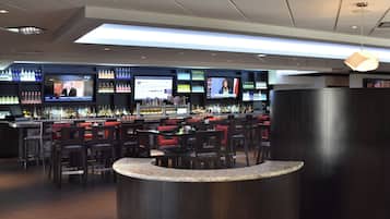 A bar area with multiple screens displaying content, a variety of liquor bottles, and seating arrangements.
