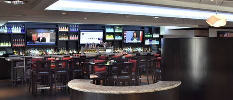 A bar area with multiple screens displaying content, a variety of liquor bottles, and seating arrangements.