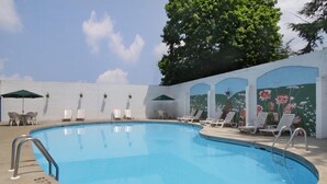 Una piscina con sillas de descanso y sombrillas, rodeada por un muro blanco con murales florales.