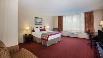 A hotel room with a large bed, two bedside tables with lamps, a desk, a chair, and a large window with curtains.