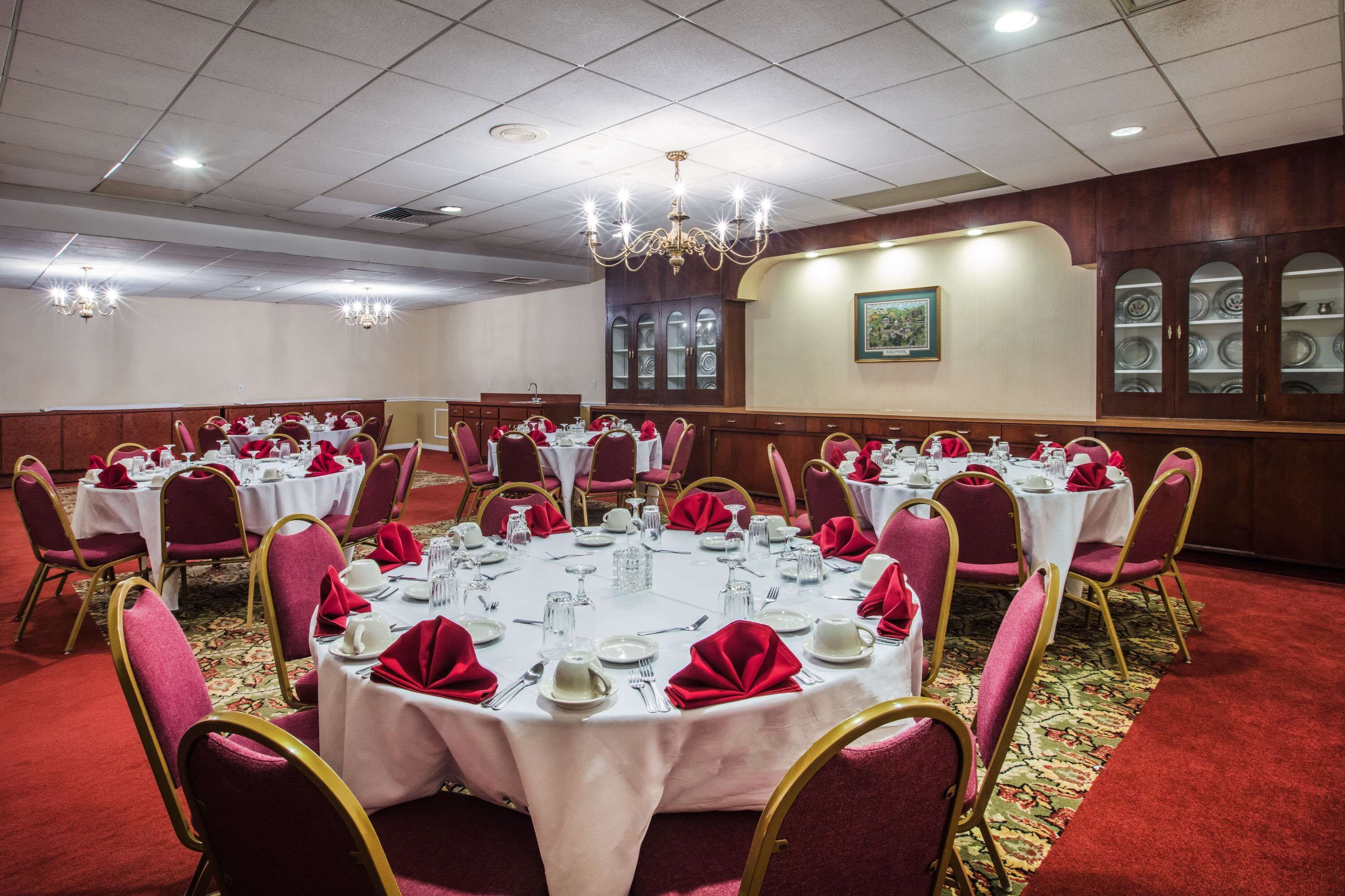 A banquet hall with round tables set for dining, each with white tablecloths and red napkins.