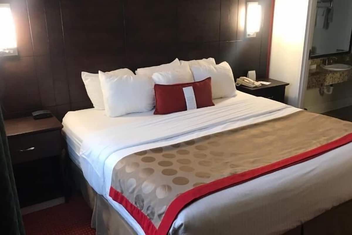 Ein Hotelzimmer mit einem Bett, einem Nachttisch mit Telefon, einem Spiegel und einem Badezimmer im Hintergrund.