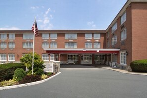 A multi-story hotel with a brick facade, a covered entrance, and an American flag. - Ramada by Wyndham Ligonier (Ligonier)