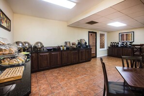 A buffet-style breakfast area with a variety of food items, a coffee station, and a seating area with a table and chairs. - Ramada by Wyndham Ligonier (Ligonier)