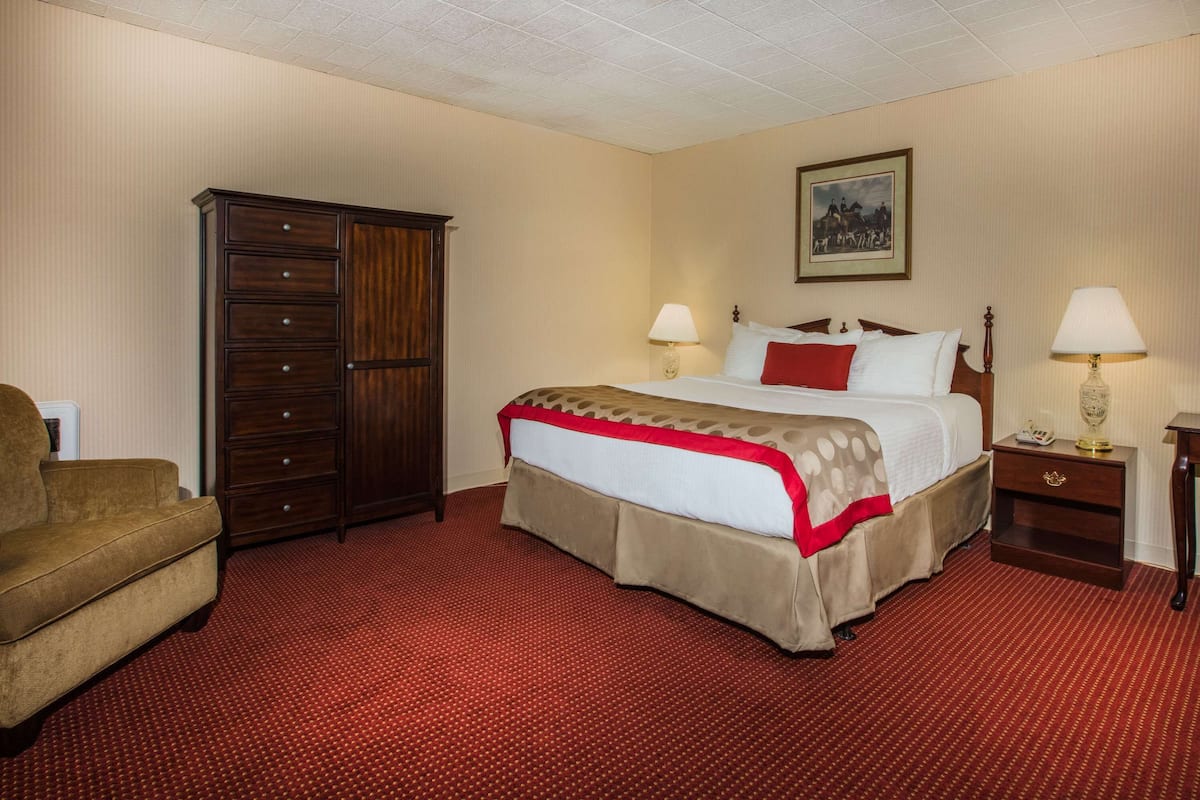 A hotel room with a large bed, two bedside tables with lamps, a wooden wardrobe, and a red carpet.