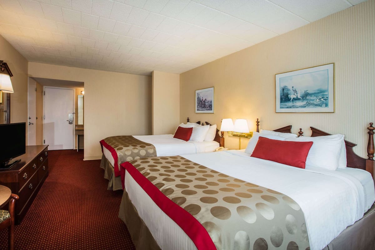 A hotel room with two beds, a TV, a desk, and a door leading to a bathroom.