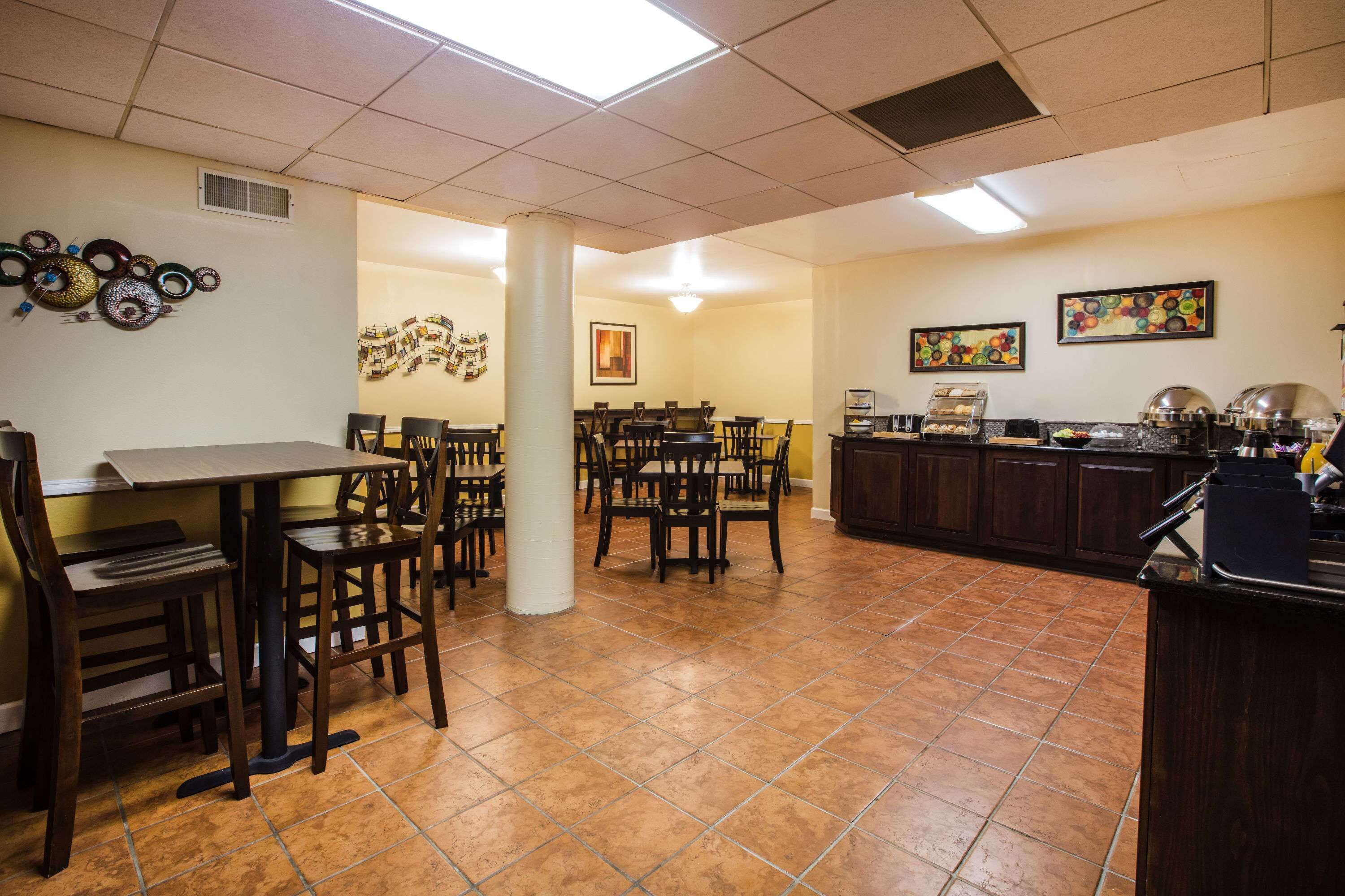 A dining area with multiple tables and chairs, a kitchen counter with food items, and decorative wall art.