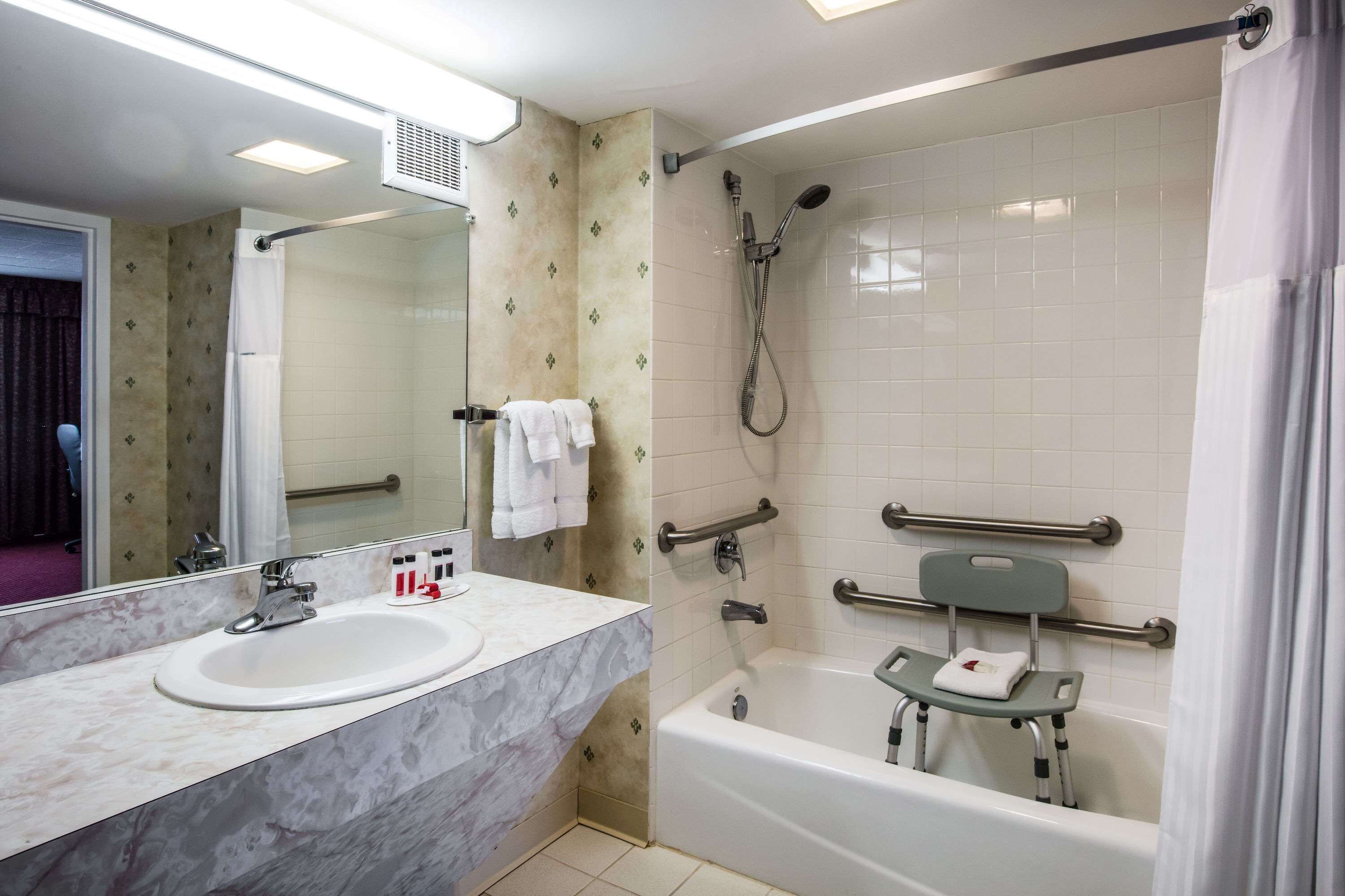 Een badkamer met een wastafel, spiegel, douche en handgrepen.