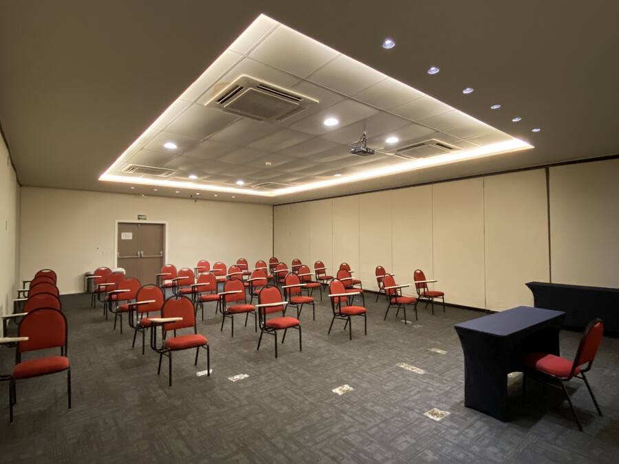 A conference room with rows of red chairs, a black table, and recessed lighting on the ceiling.