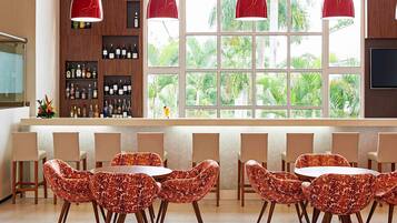 A bar area with a large window, multiple shelves of bottles, and a seating arrangement with patterned chairs.
