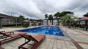 Una piscina con sillas de descanso y sombrillas, rodeada de palmeras y un edificio que dice "NOVOTEL".