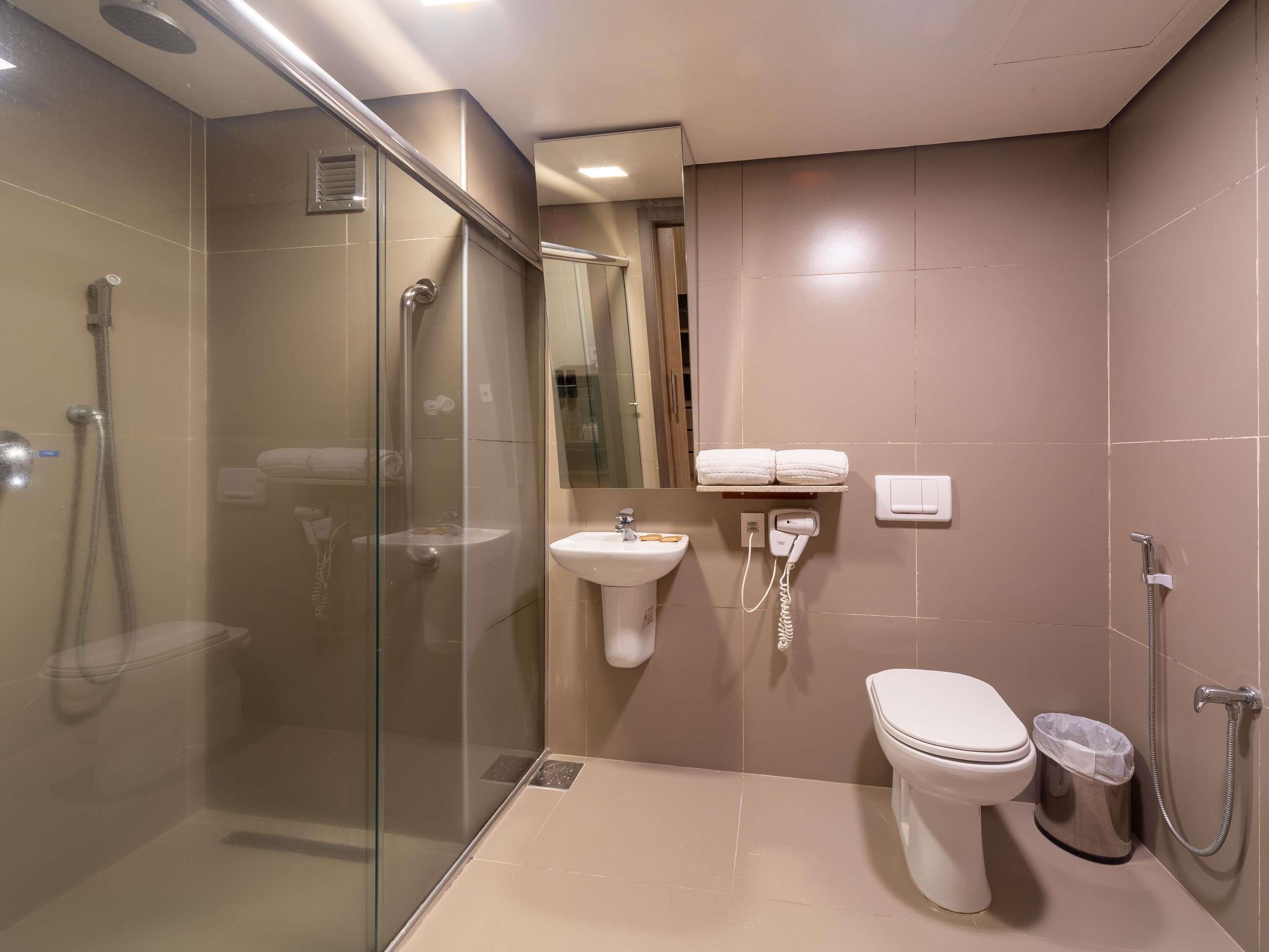 Un bagno moderno con doccia vetrata, lavabo a piedistallo, water e porta asciugamani con asciugamani.