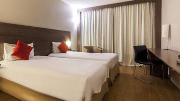 A hotel room with two beds, a desk, a chair, and a large window with curtains.