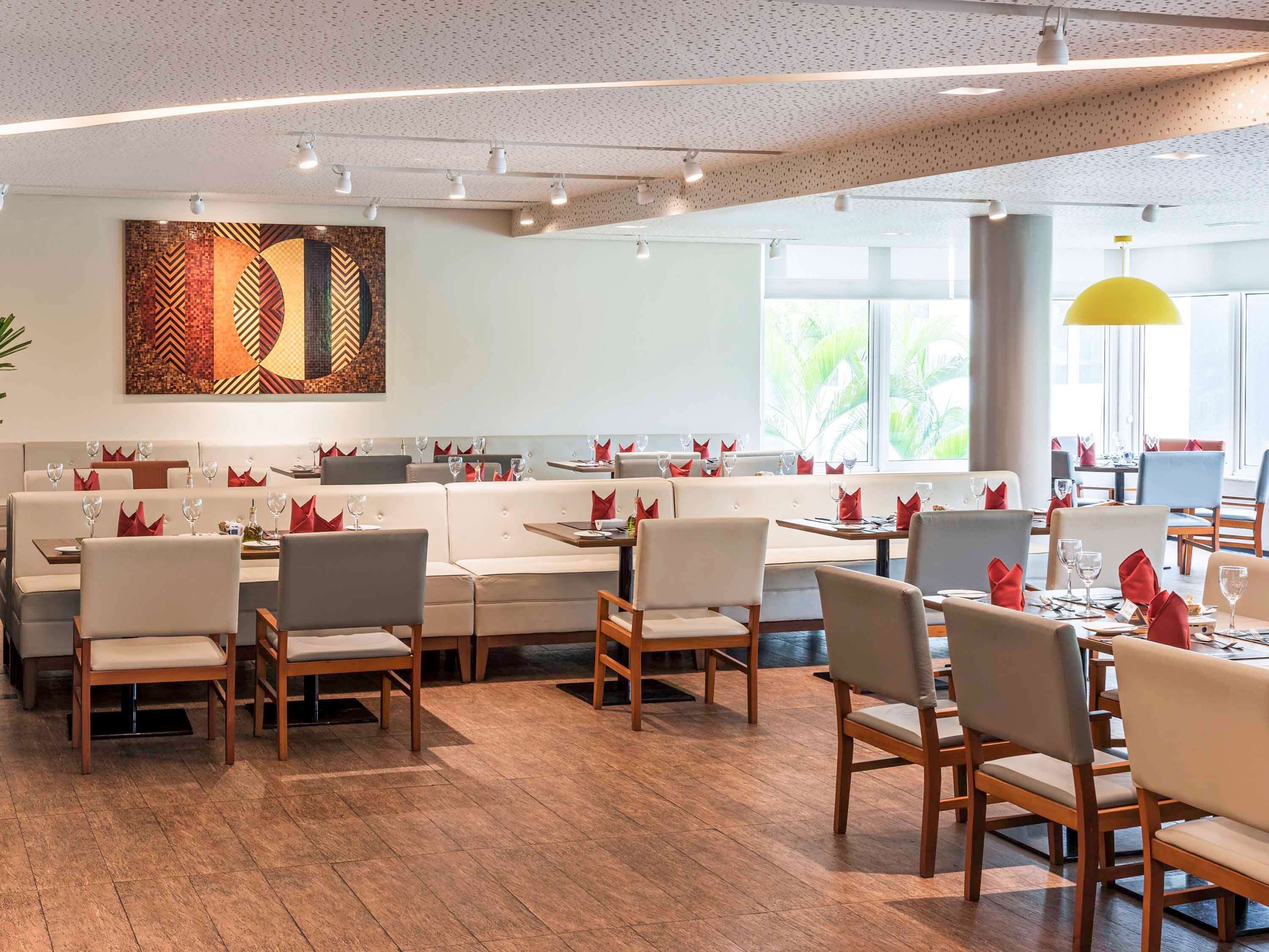 Un restaurant moderne avec des banquettes et des tables en bois, agrémenté d’une grande œuvre d’art abstrait au mur et de grandes fenêtres laissant entrer la lumière naturelle.