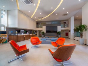 Un vestíbulo moderno con mostrador de recepción, zona de estar y una escalera que conduce a un nivel superior.