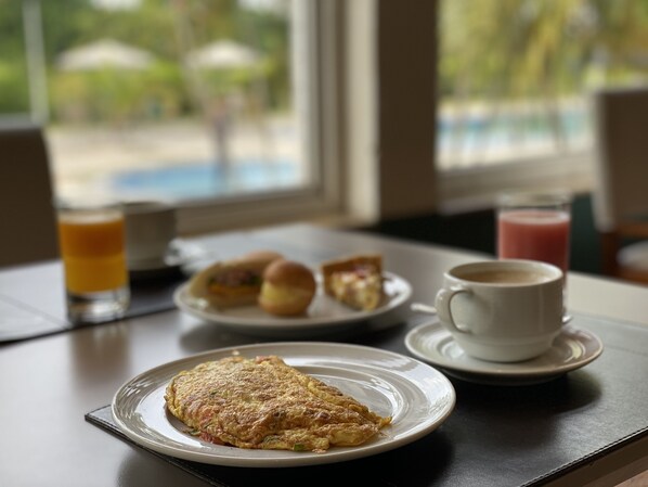 Desayuno servido en una mesa junto a una ventana, con un plato de comida, una taza de café y un vaso de jugo de naranja.