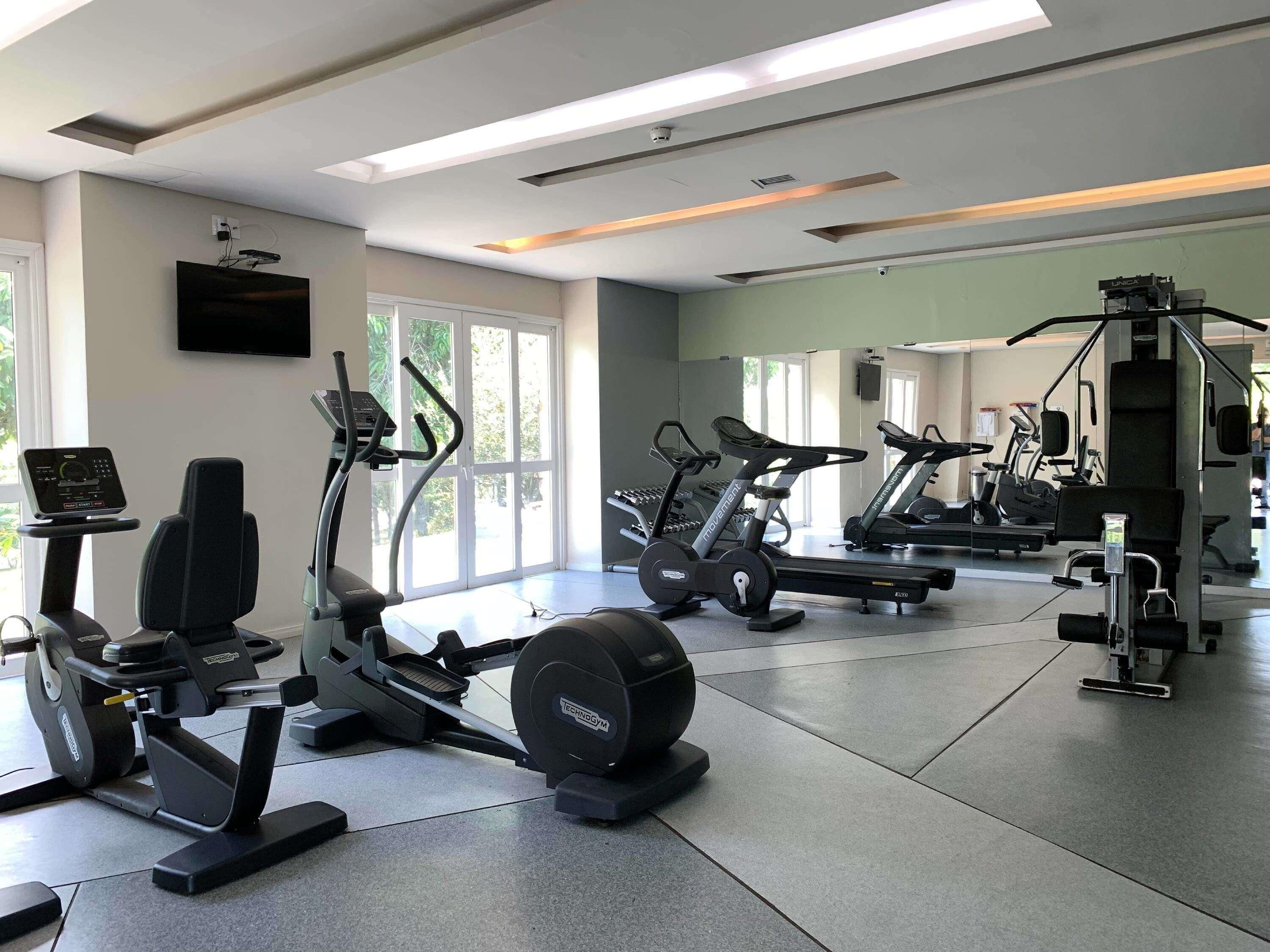 Un gimnasio con máquinas de cardio, equipo de pesas y un espejo grande.