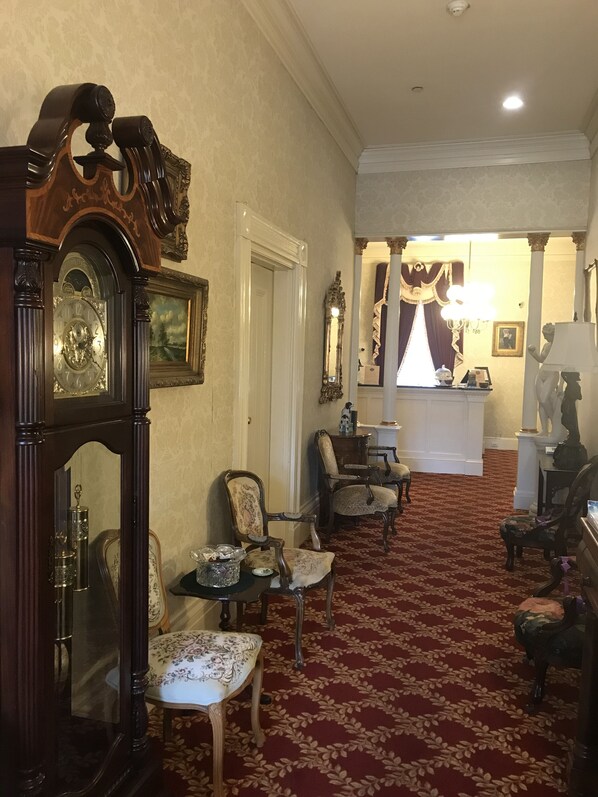 A formal room with a red carpet, wooden furniture, and a large grandfather clock.
