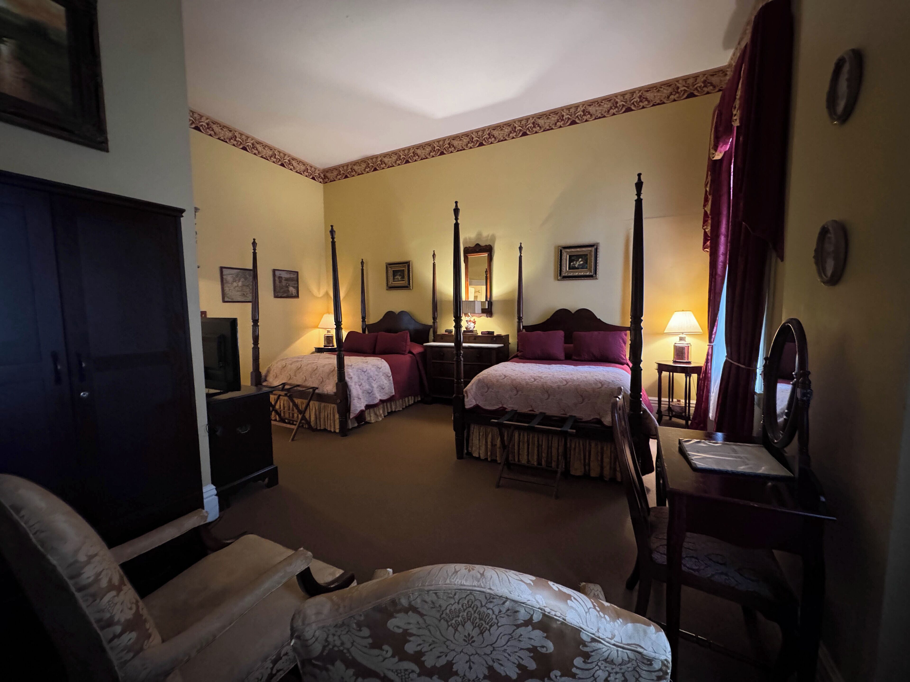 A four-poster bed with a canopy, a desk with a mirror, and a chair in a hotel room.