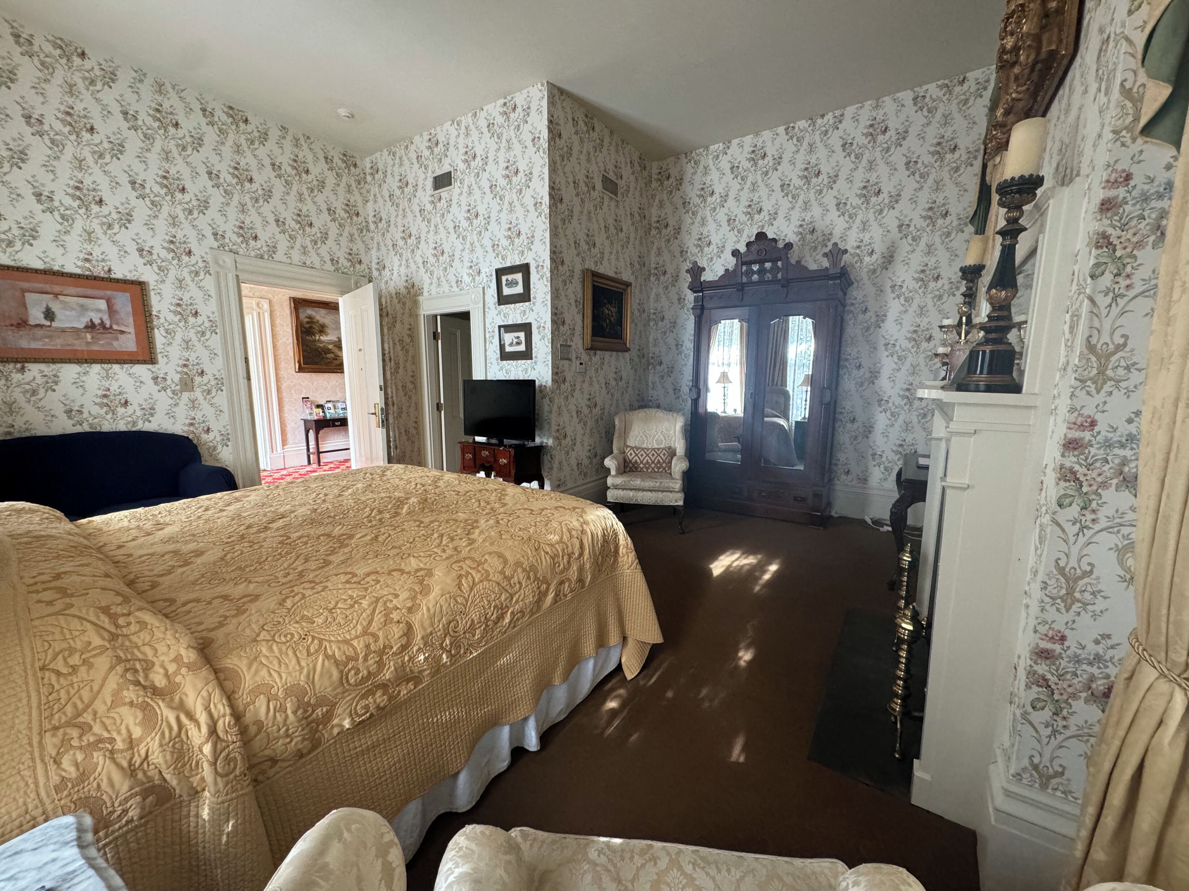 Una habitación con una cama grande, un armario de madera, una silla y un televisor.