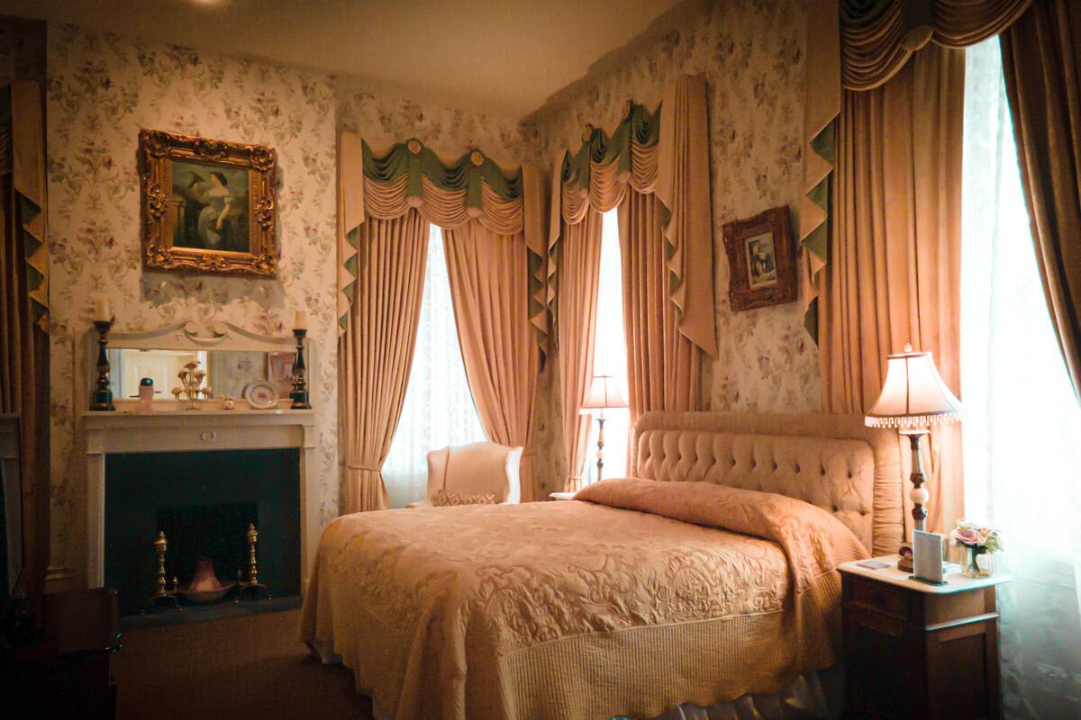 A classic bedroom with a fireplace, a bed with a tufted headboard, and curtains.