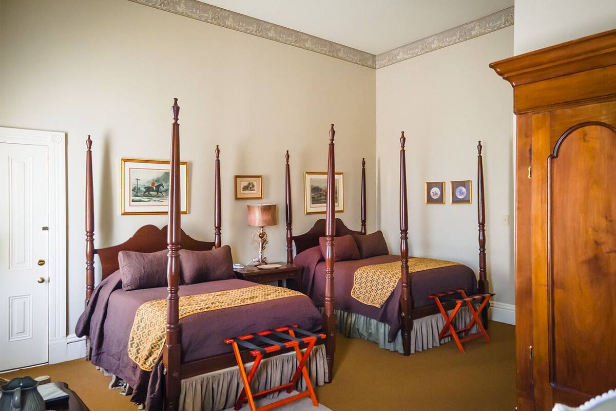 A traditional four-poster bed room with two beds, a wooden wardrobe, and a door.