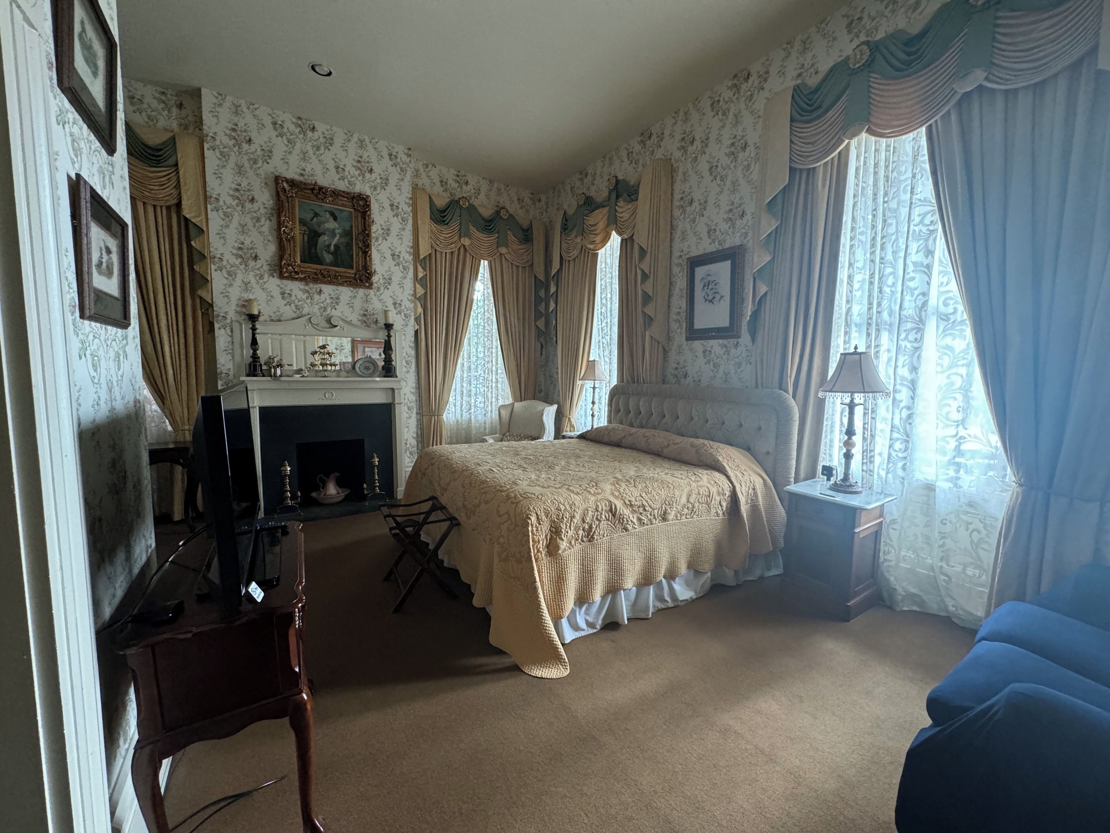 Een slaapkamer met een groot bed, een open haard, een bureau en een blauwe fauteuil.