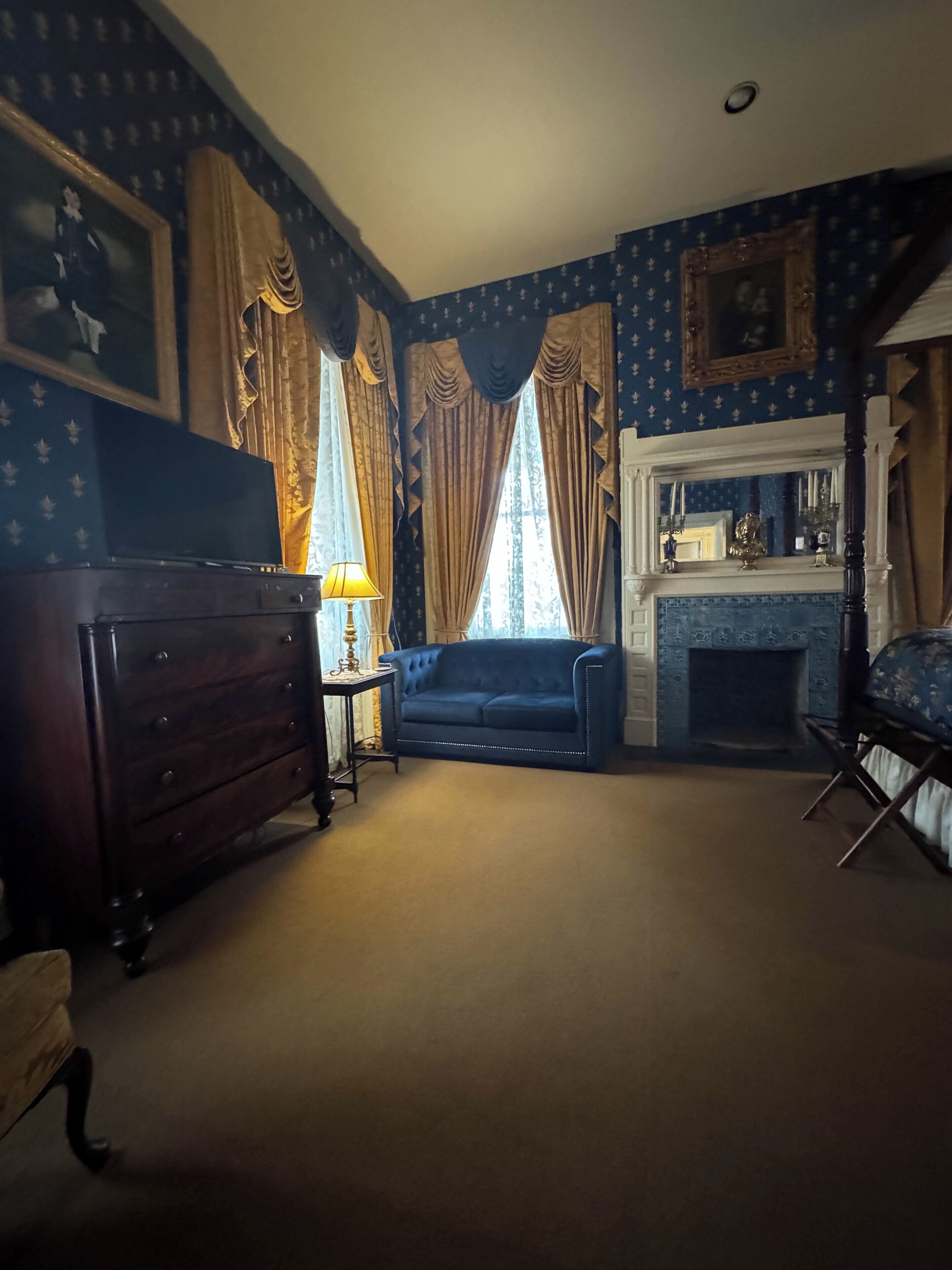 Une pièce avec une cheminée, un canapé bleu, une commode en bois et des rideaux.
