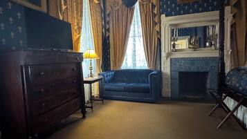 A room with a fireplace, a blue sofa, a wooden dresser, and curtains.