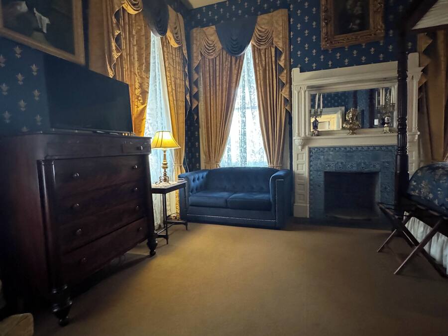 A room with a fireplace, a blue sofa, a wooden dresser, and curtains.