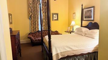 A four-poster bed with a canopy, a wooden dresser, a chair, and a bedside table with a lamp.