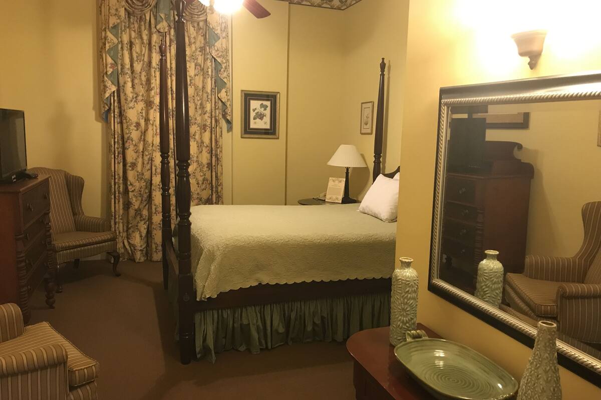 A hotel room with a bed, a dresser, a chair, a mirror, and a lamp.