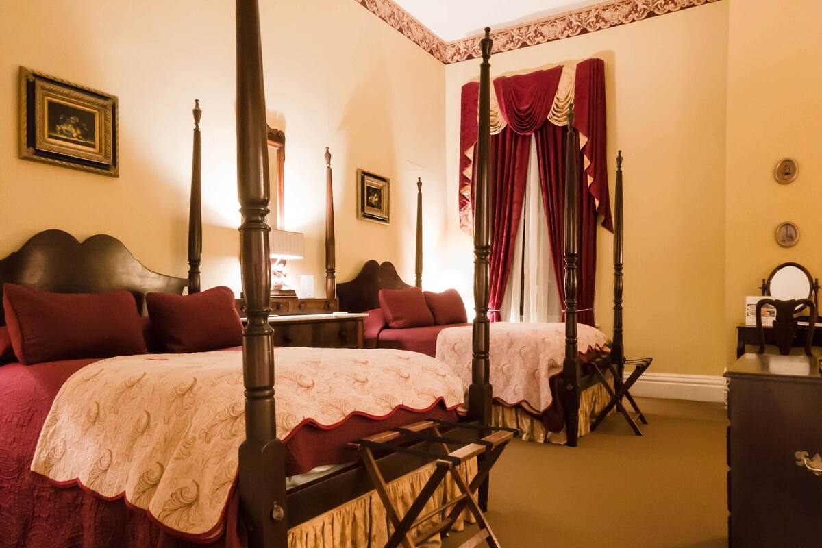 A four-poster bed with a canopy, two bedside tables, a dresser, and a chair.