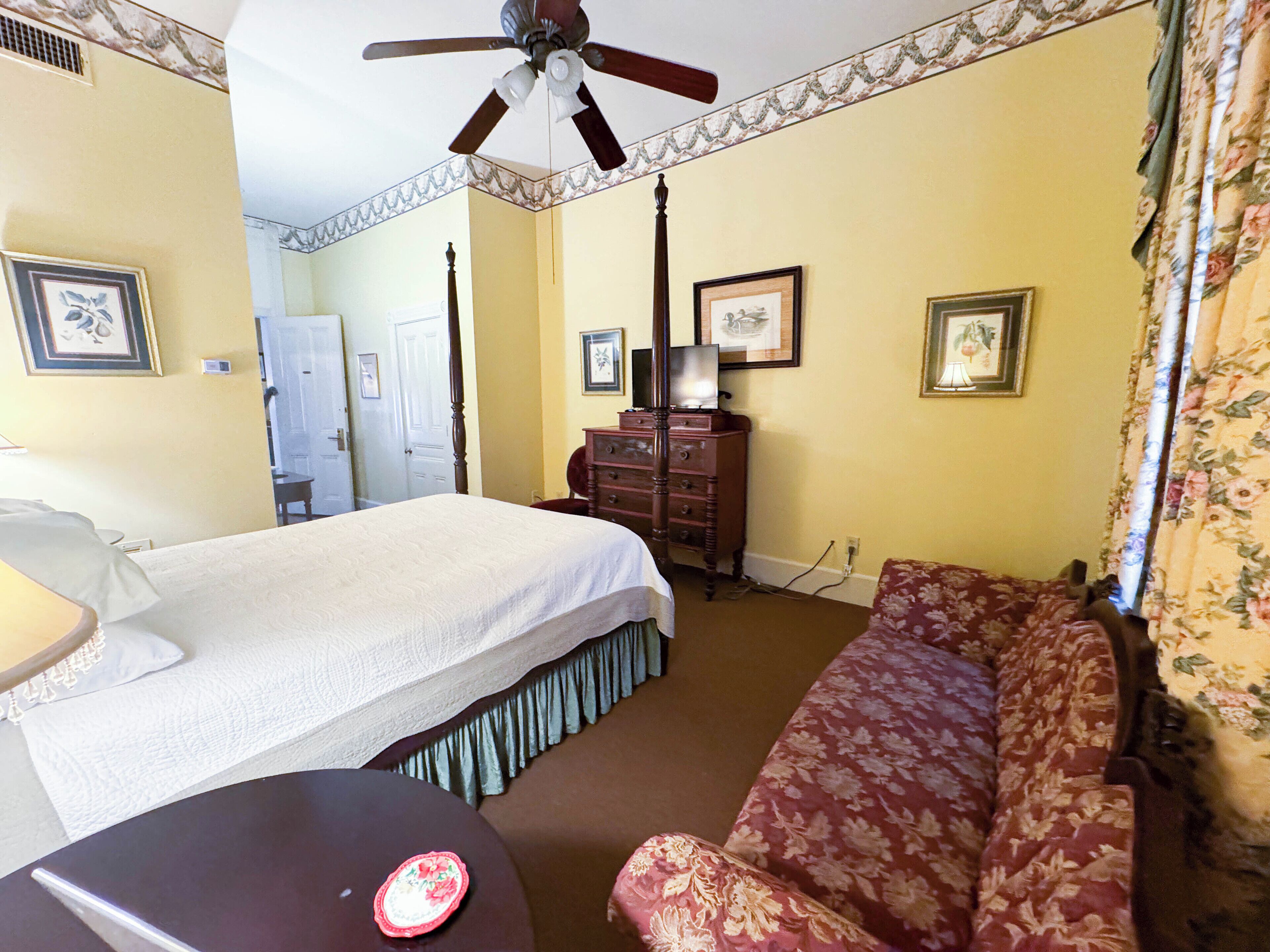 A hotel room with a bed, a sofa, a dresser, and a ceiling fan.