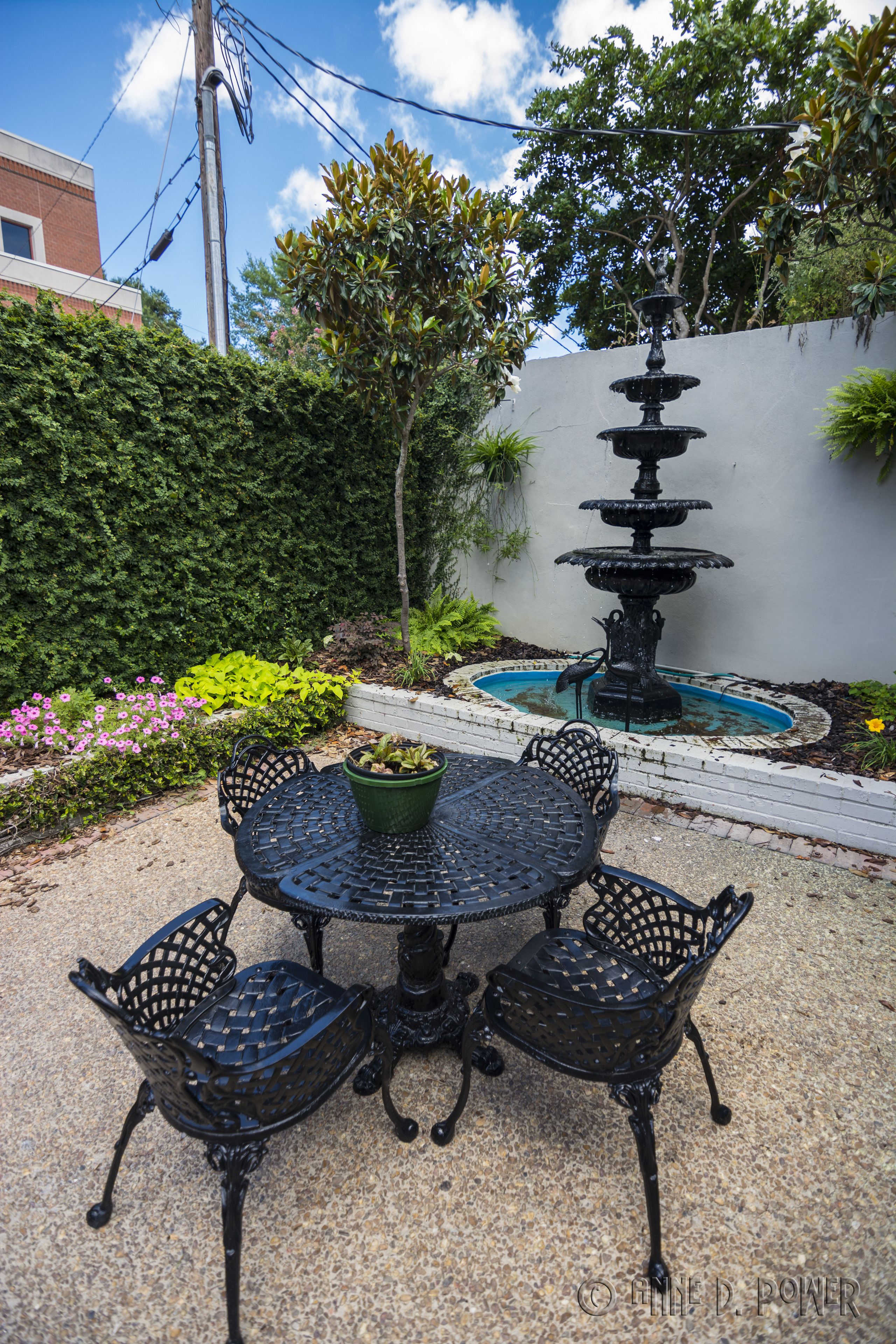 A patio with a round table and four chairs, surrounded by a garden with a fountain and various plants.