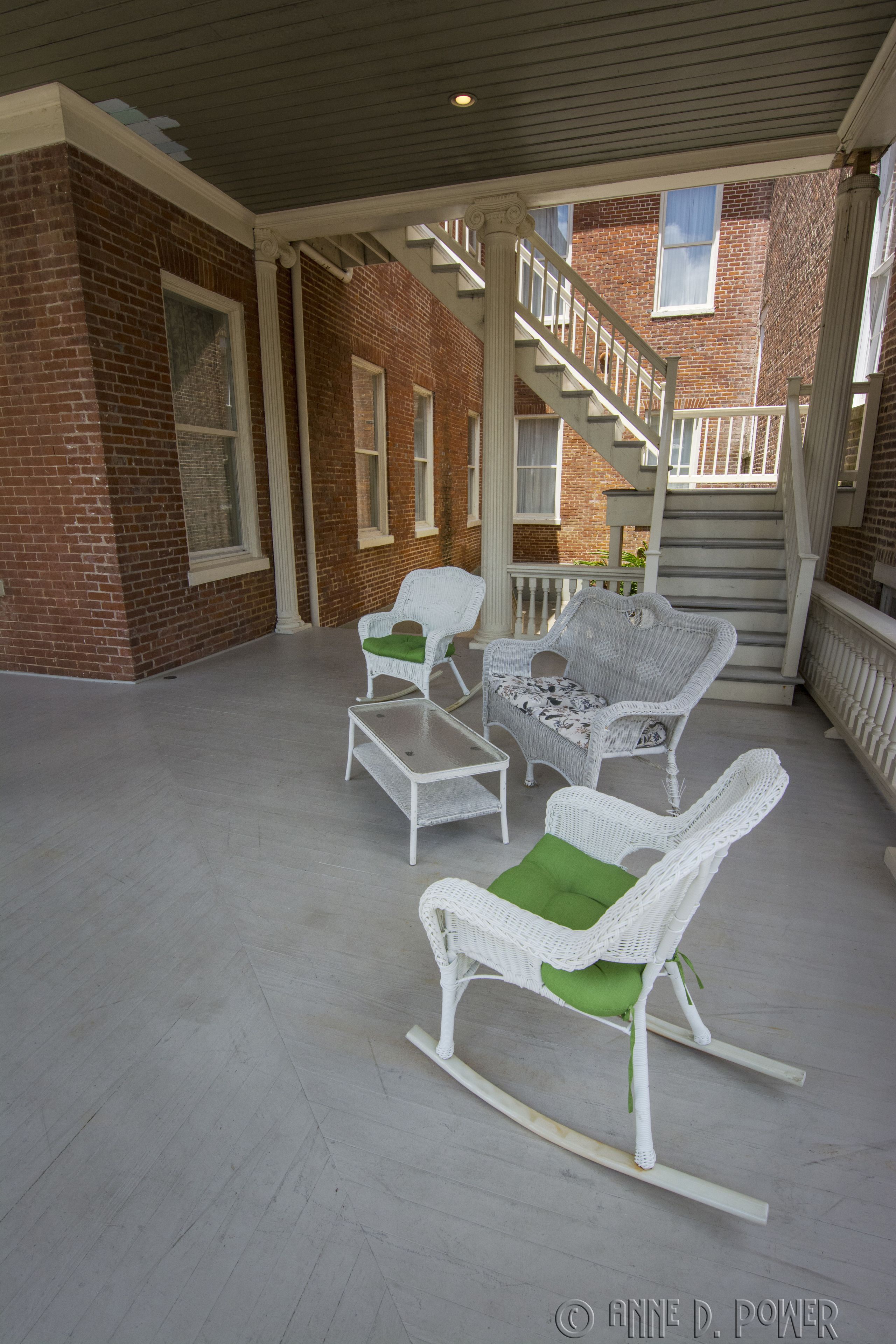 Un patio techado con muebles de mimbre blanco y un edificio de ladrillo al fondo.