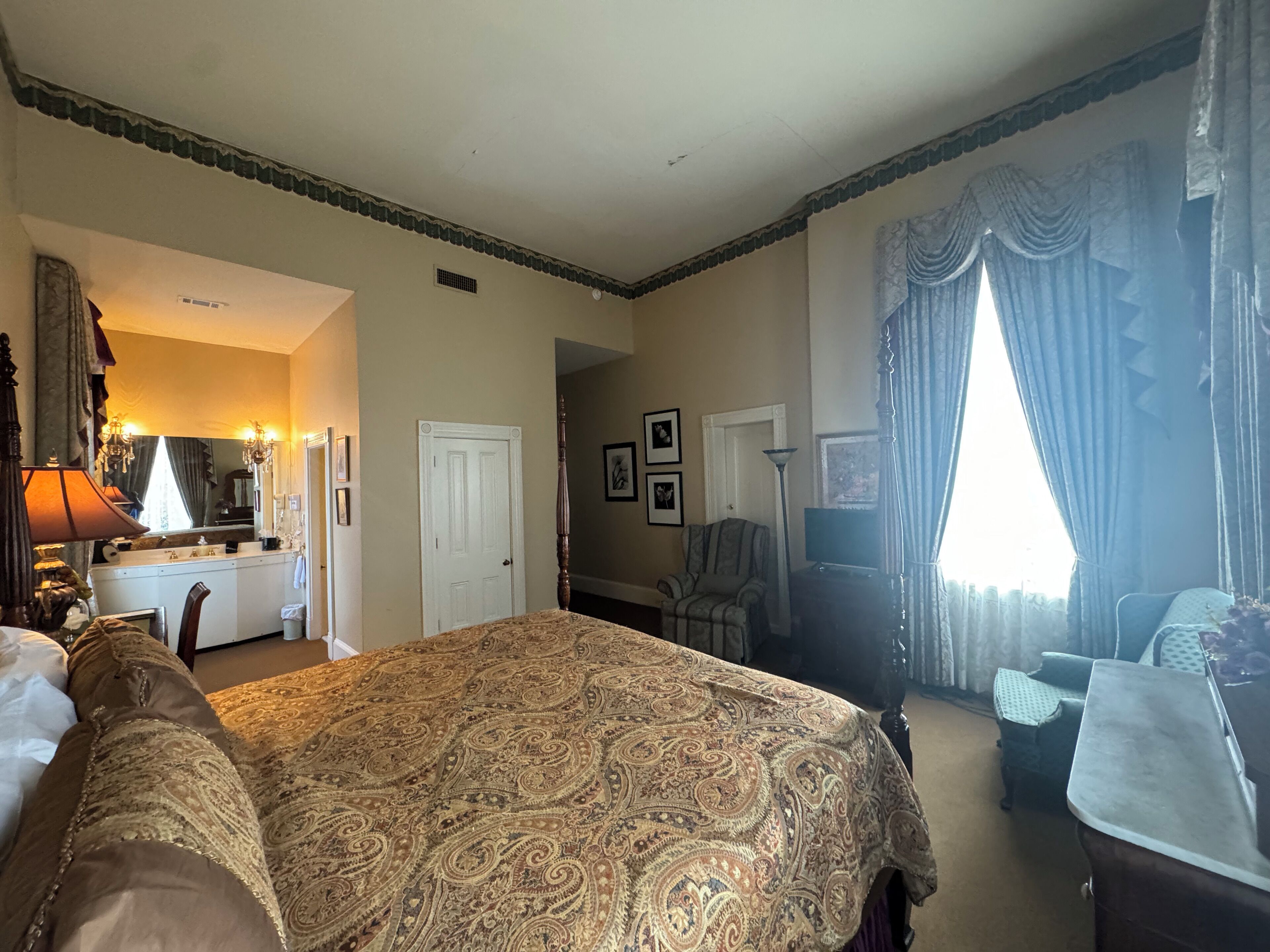 Habitación de hotel con una cama grande, un escritorio, una silla, un tocador con espejo y una ventana con cortinas.