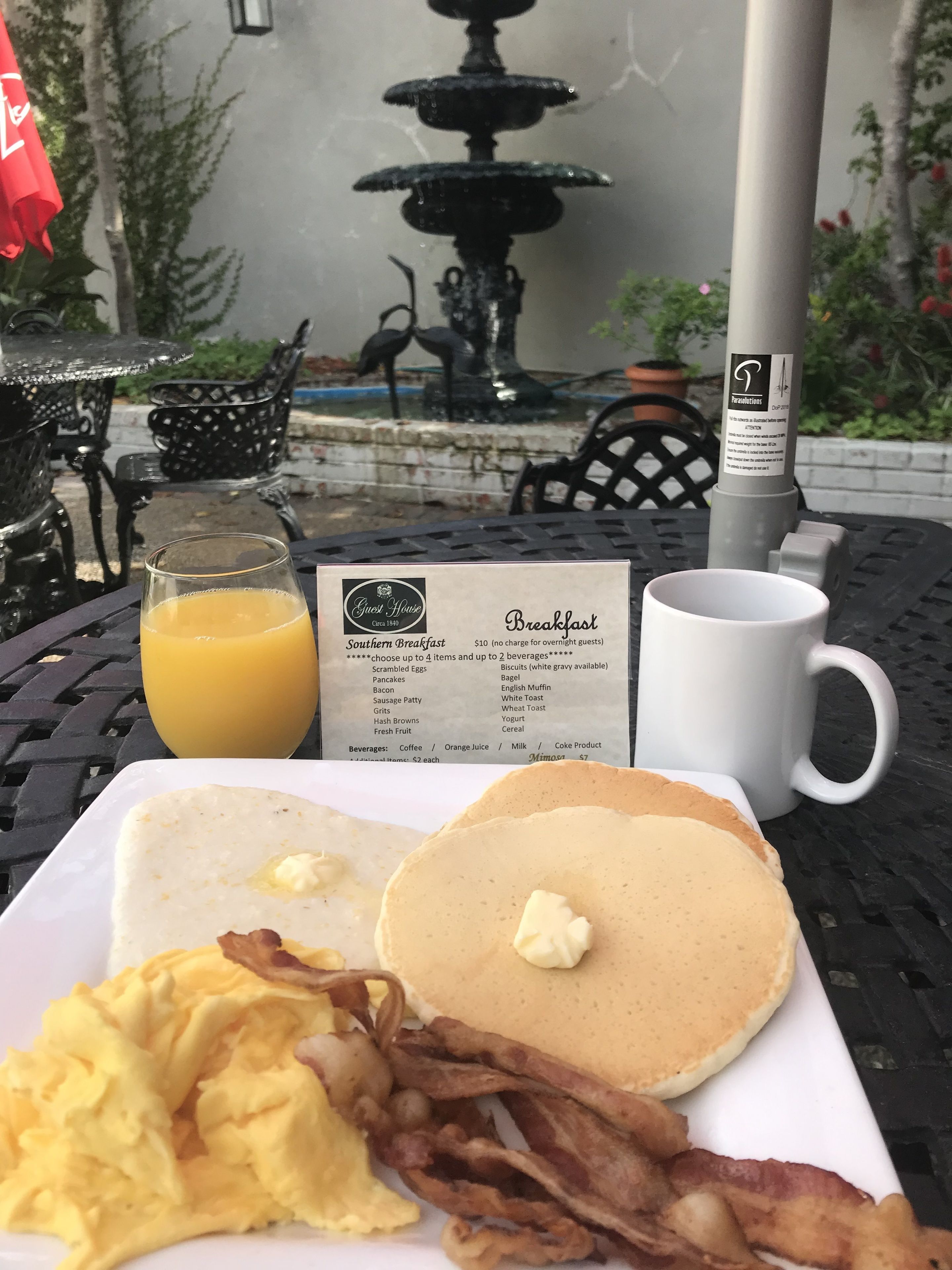 A breakfast setting with scrambled eggs, bacon, pancakes, and orange juice on a table.