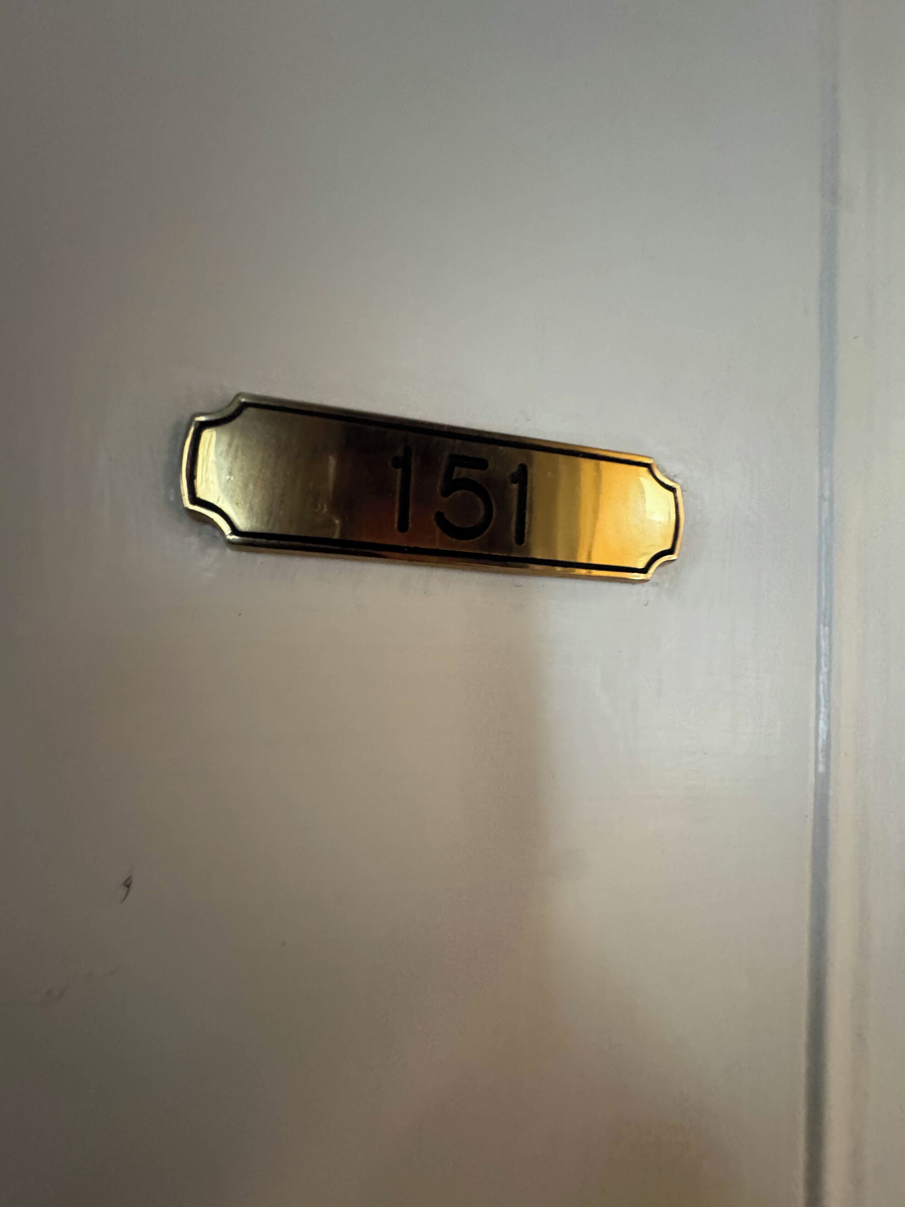 Een koperen deurplaat met het nummer 151.