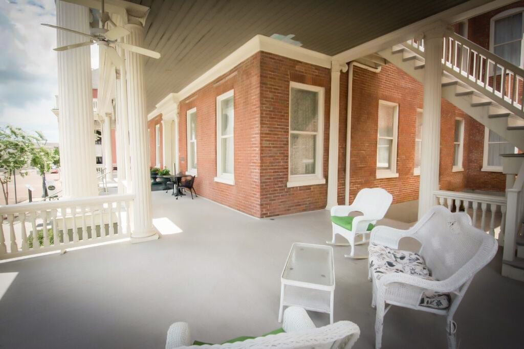 A covered porch with white wicker furniture, brick walls, and a white railing.