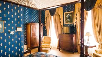 Una habitación con una cama con dosel, un aparador de madera, una silla y una mesa con lámpara.