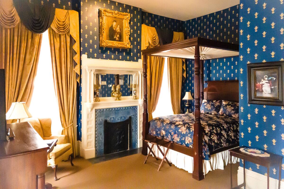 A bedroom with a four-poster bed, a fireplace, and a portrait on the wall.