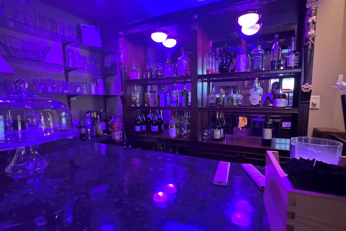 A bar area with shelves of liquor bottles, a marble countertop, and overhead lighting.