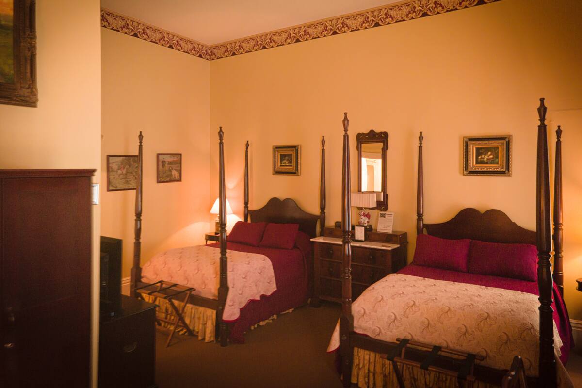 A traditional four-poster bed room with two beds, a nightstand, and a dresser.