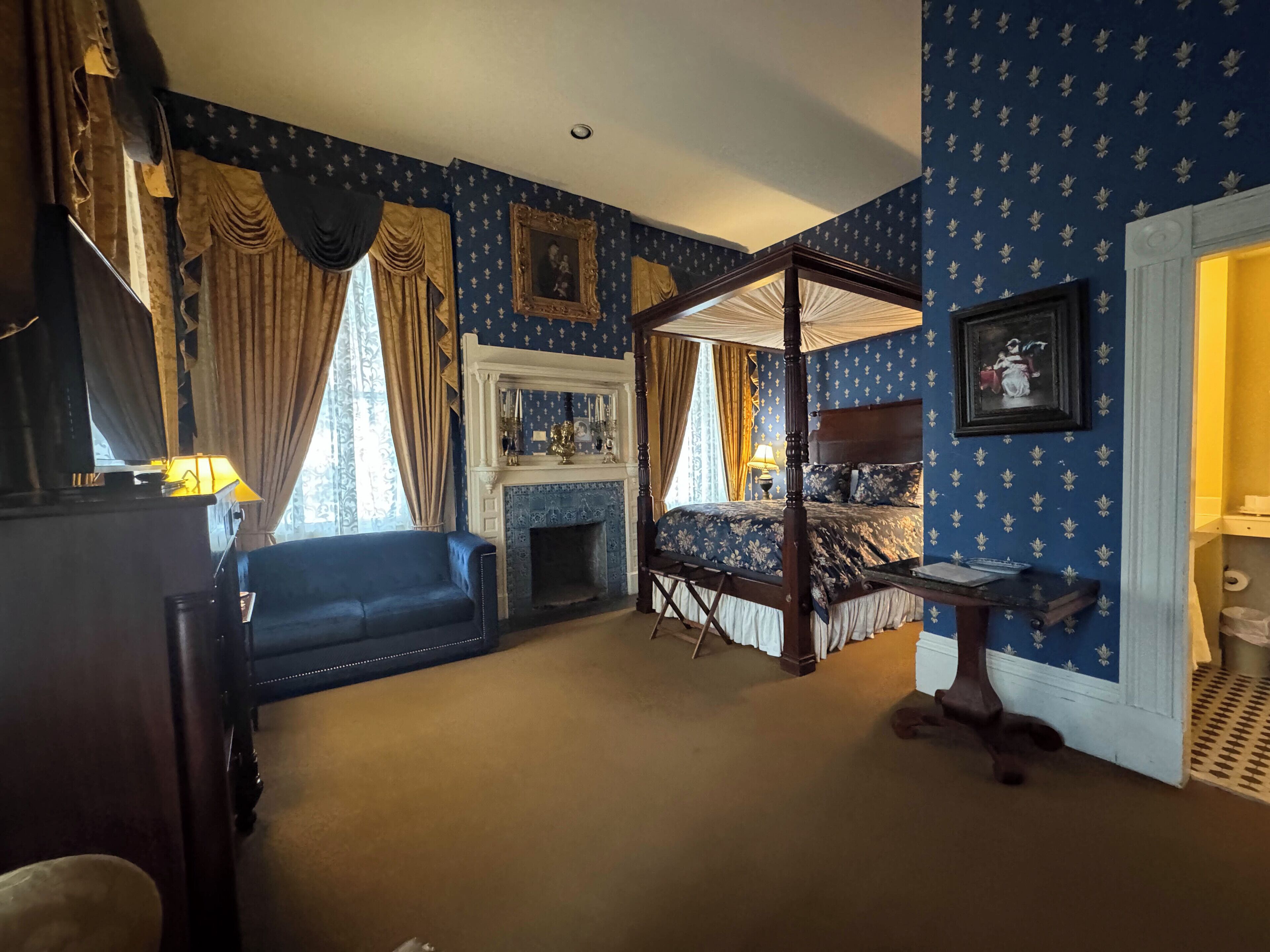 A room with a four-poster bed, a fireplace, and a blue patterned wallpaper.