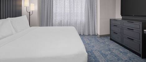 A hotel room with a large bed, a flat-screen TV, a dresser, and a window with curtains.