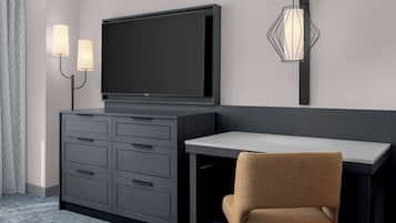 A modern hotel room with a flat-screen TV, a desk, and a chair. There are two wall-mounted lamps and a unique wall light fixture.