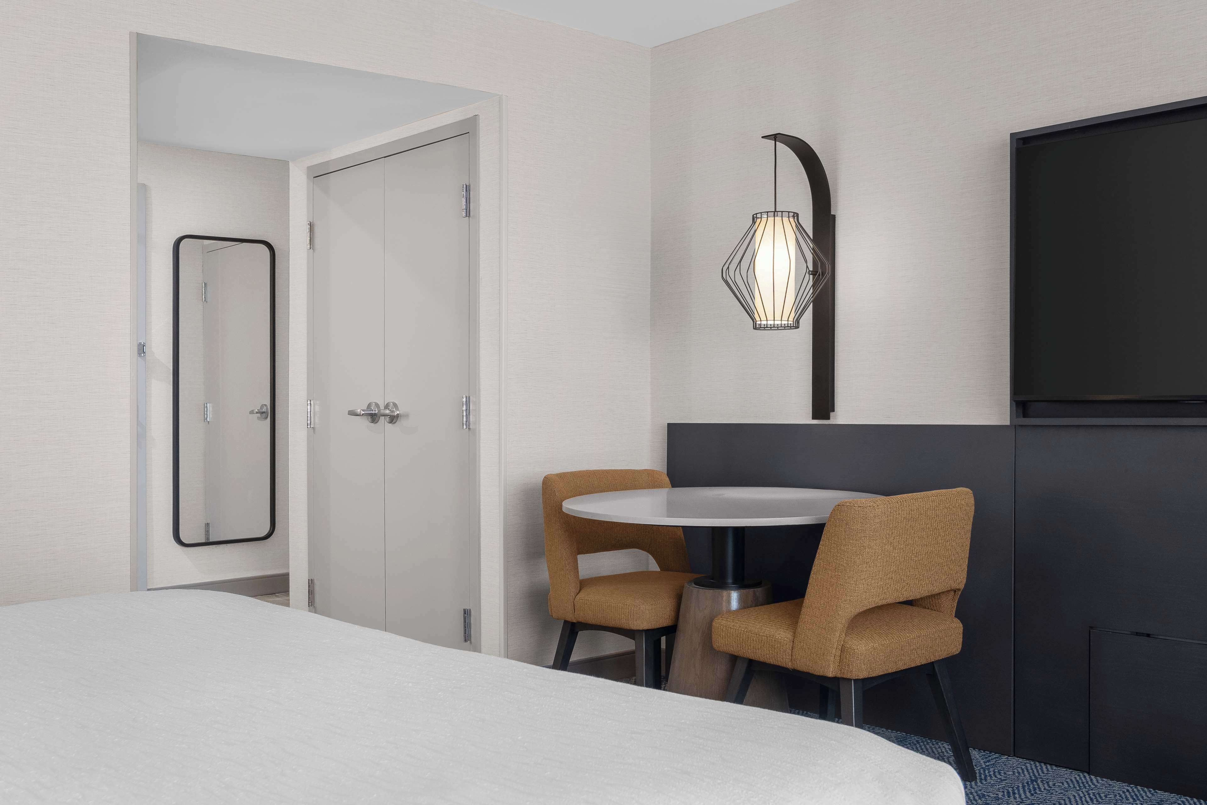 A hotel room with a bed, a round table with two chairs, a TV, and a wall-mounted light fixture.