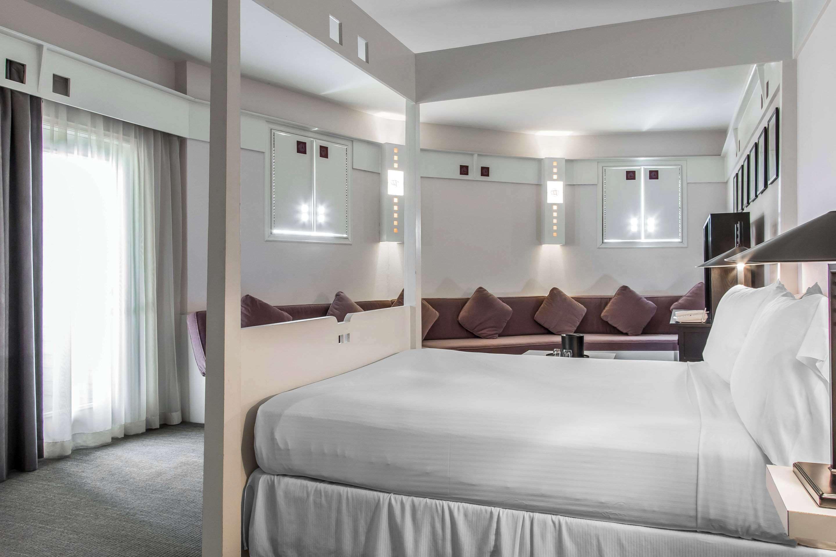 A hotel room with a large bed, a sofa, a desk, and a mirror.