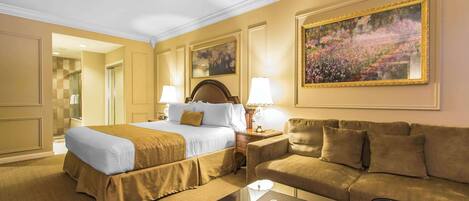 A hotel room with a bed, a sofa, a coffee table, and a painting on the wall.